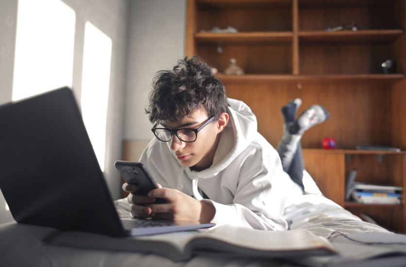 young boy studies lying on the bed using computer and smartphone Rapport de l’Observatoire : Les jeunes et l’addiction aux écrans