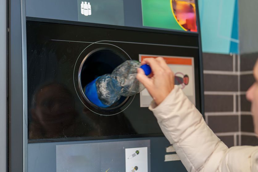 Person recycling a plastic bottle at a modern recycling station inside a city environment Le débat sur la consigne plastique relancé